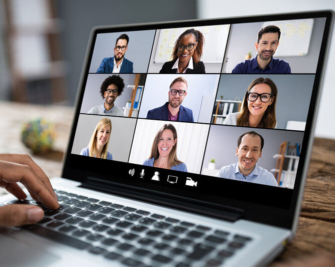 Laptop screen showing a video call with multiple participants on a wooden desk.
